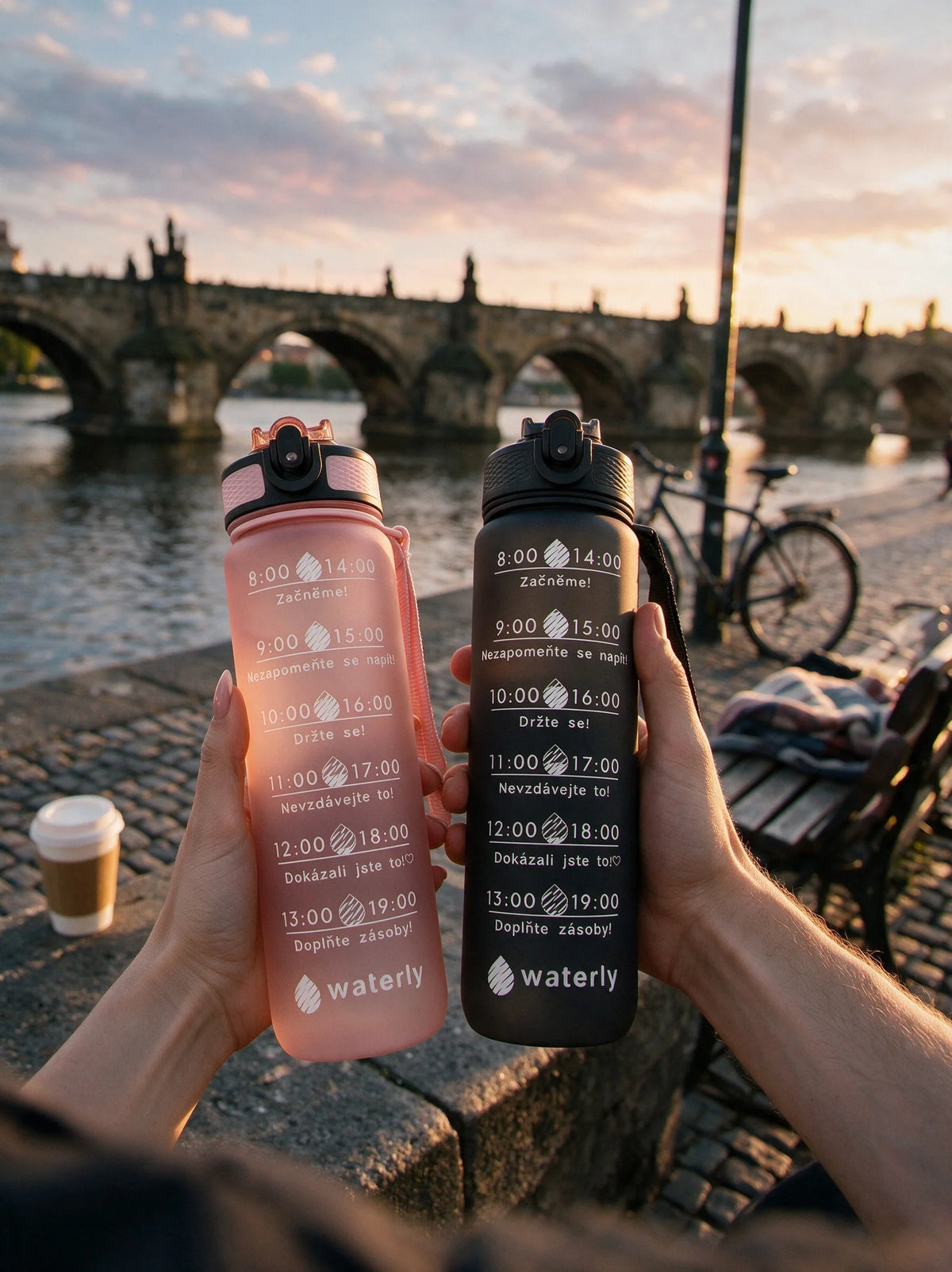 Pár drží motivační láhve Waterly při západu slunce, Karlův most v pozadí